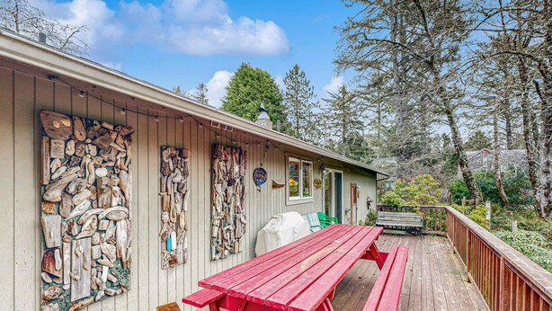 A wooden deck with a red picnic table, a covered grill, and a wooden wall with various objects. - Dog-Friendly Cottage with Private Hot Tub, Deck, Berry Bushes, & Beach Access (Cannon Beach)