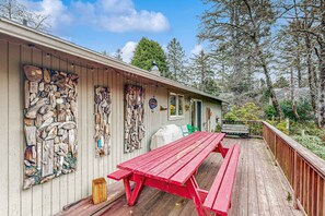 A wooden deck with a red picnic table, a covered grill, and a wooden wall with various objects. - Dog-Friendly Cottage with Private Hot Tub, Deck, Berry Bushes, & Beach Access (Cannon Beach)