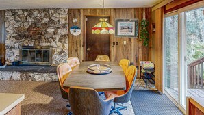 A dining room with a stone wall, wooden paneling, a chandelier, and a large window. - Dog-Friendly Cottage with Private Hot Tub, Deck, Berry Bushes, & Beach Access (Cannon Beach)
