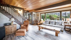 A spacious living room with a wooden staircase, a sofa set, a coffee table, and a view through large windows. - Dog-friendly, oceanfront home just a stroll from the beach and shopping & dining (Cannon Beach)