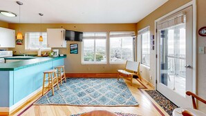 A kitchen with a blue island, wooden stools, a patterned rug, and a large window with a view. - Oceanfront Nye Beach condo with gorgeous corner view & beach access (Newport)
