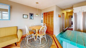 A dining area with a round table, white chairs, a yellow sofa, and a patterned rug. - Oceanfront Nye Beach condo with gorgeous corner view & beach access (Newport)