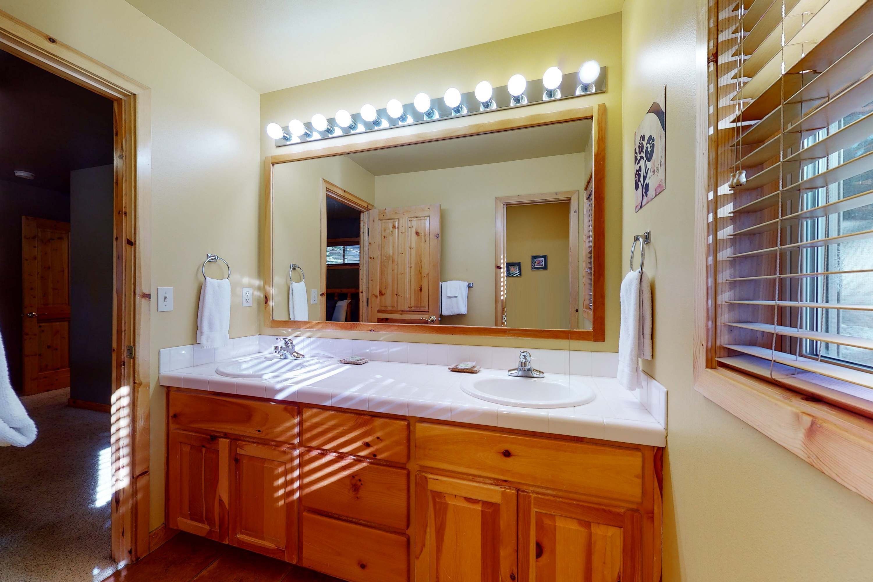 Une salle de bain avec des meubles en bois, un double vasque et un grand miroir avec éclairage intégré.