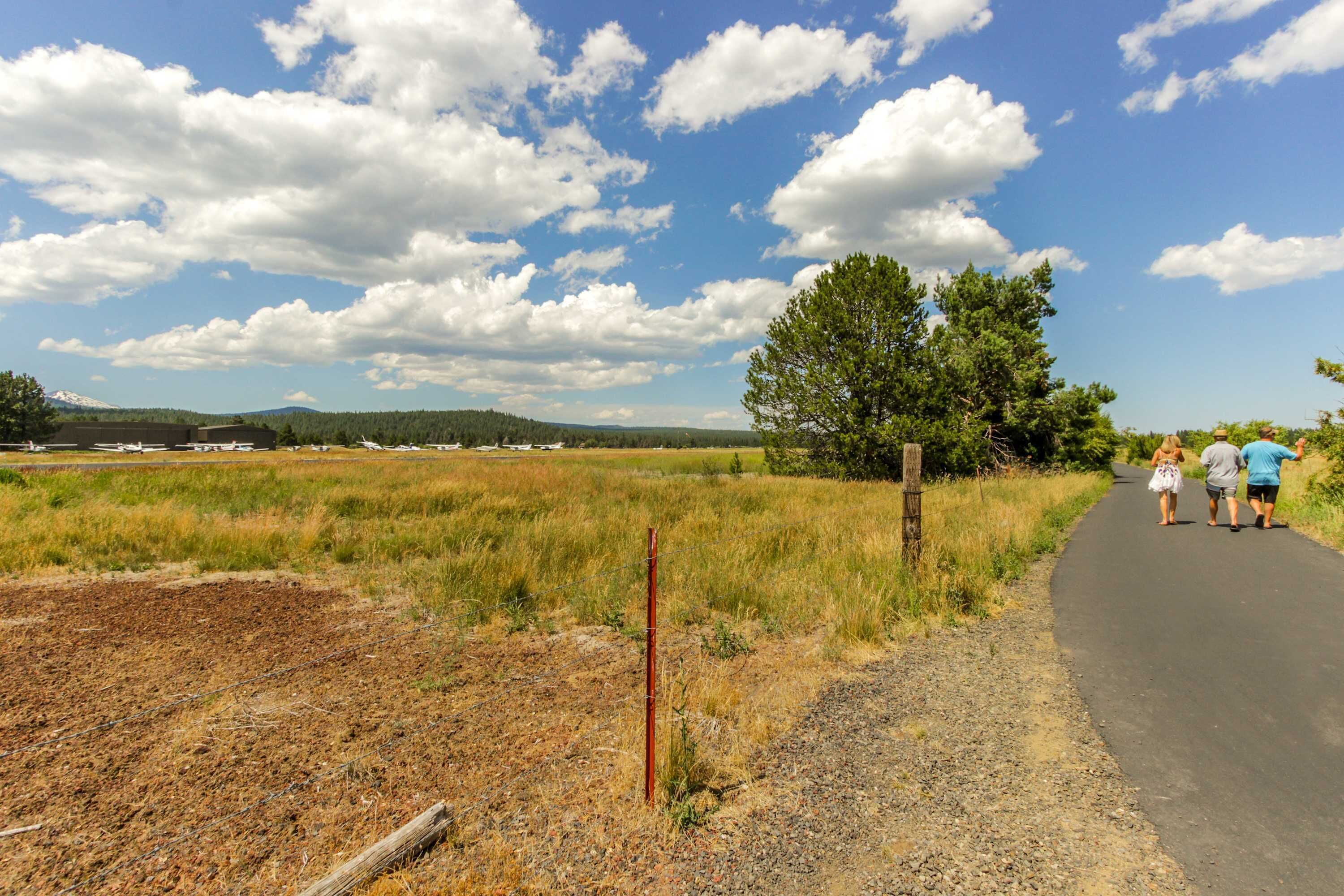 A rural landscape with a paved path, open fields, and a clear sky.