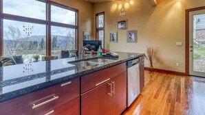 Une cuisine dotée d’un grand îlot central, de meubles en bois, d’un lave-vaisselle et offrant une vue sur les montagnes grâce à de grandes fenêtres.