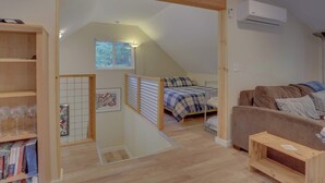 Un dormitorio estilo loft con techo inclinado, una cama con colcha azul y blanca a cuadros, un sofá marrón, una estantería de madera y una pequeña mesa.