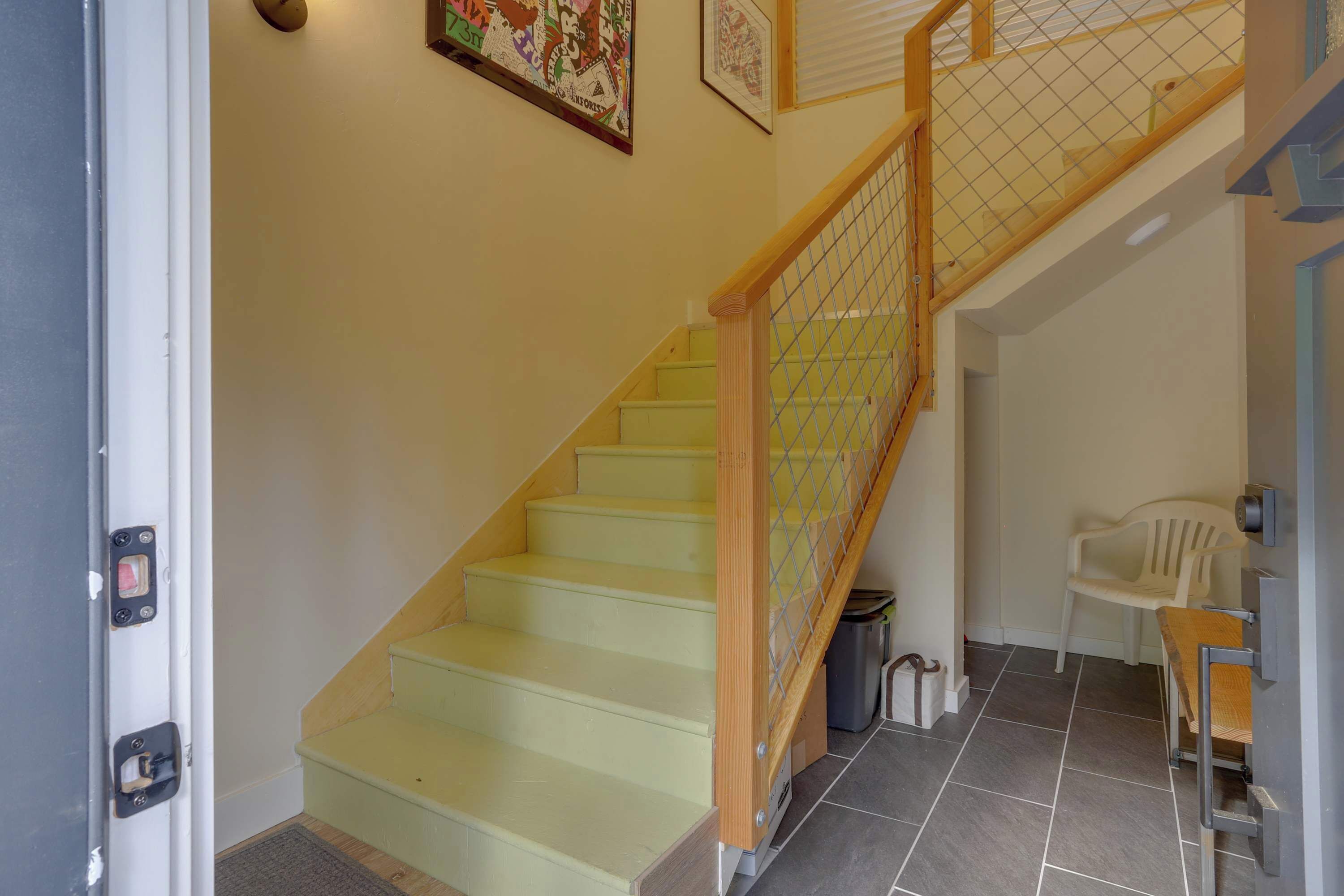 A staircase with a wooden handrail and a metal safety railing, a white plastic chair, a trash can, and a door with a handle.