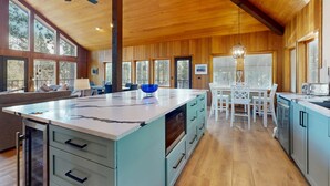 A spacious kitchen with a large island, wooden ceiling, and large windows. - Whimsical tree-lined stay with wood stove, AC, shared amenities, and large deck (Black Butte Ranch)