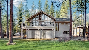 A two-story cabin with a balcony, surrounded by tall trees. - Whimsical tree-lined stay with wood stove, AC, shared amenities, and large deck (Black Butte Ranch)