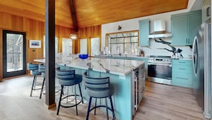 A spacious kitchen with wooden beams, a large island with bar stools, and modern appliances. - Whimsical tree-lined stay with wood stove, AC, shared amenities, and large deck (Black Butte Ranch)