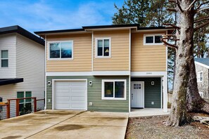 A two-story residential building with a garage, a small porch, and a tree in the foreground. - Charming home with ocean views, patio, BBQ grill, WiFi, W&D, walk to beach (Cannon Beach)