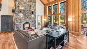 Ein gemütliches Wohnzimmer mit Kamin aus Stein, Ledersofa und großen Fenstern mit Blick ins Freie.