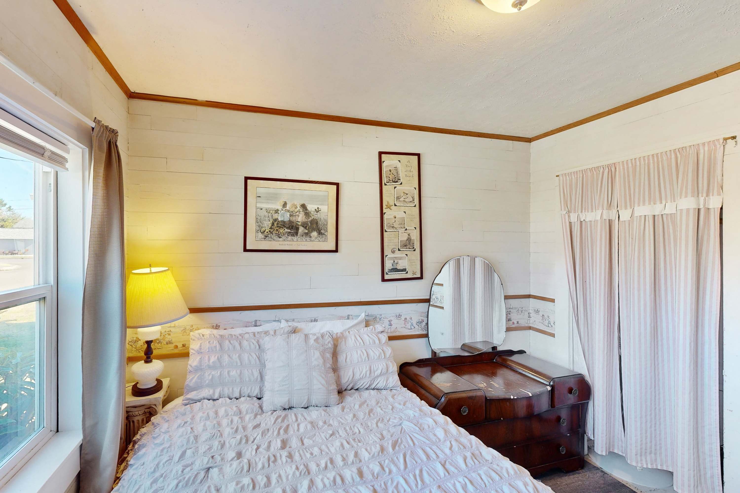 A hotel room with a bed, a bedside lamp, a dresser, a mirror, and a window with curtains.