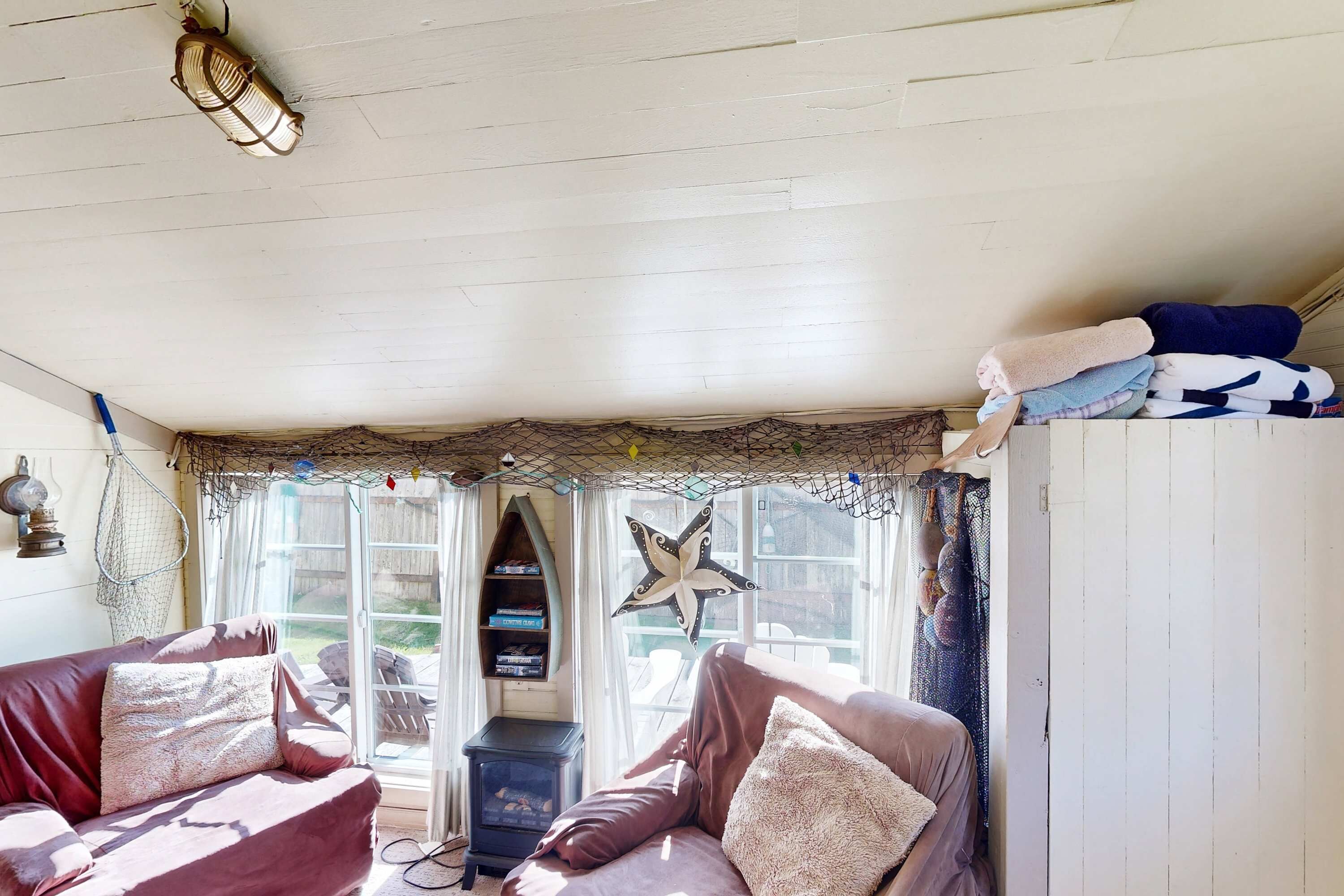 Une pièce chaleureuse avec un plafond en bois, une décoration en forme d’étoile de mer, un canapé avec des coussins et une fenêtre avec des rideaux.