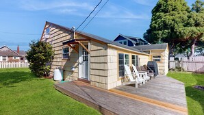 Ein Haus mit einer Holzdielen-Terrasse, einer überdachten Veranda und einem umzäunten Garten.