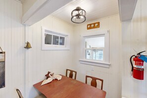 A room with white paneled walls, a wooden table with chairs, two windows, a wall-mounted fire extinguisher, and a ceiling light fixture. - Dog-friendly cottage with fireplace & enclosed yard - walk to beach/eateries (Long Beach)