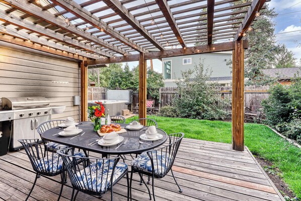 Eine Terrasse im Freien mit Holzdeck, einem runden Esstisch und einem Grill.