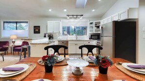 A modern kitchen with white cabinets, a black refrigerator, and a dining area with a wooden table set for four. - w/ private hot tub & easy access to downtown Bend (Bend)