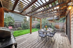 Eine Holzterrasse mit einer Pergola, einem Gartentisch und Stühlen sowie einem Grill.