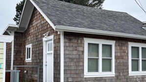A single-story house with a grey shingle exterior, white trim, and a front porch with steps. - Seaside cottage with deck, washer&dryer, full kitchen, & great location (Newport)