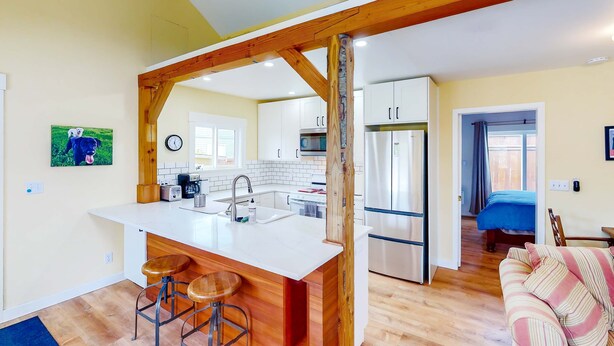 A modern kitchen with white cabinets, a central island with stools, and a wooden ceiling structure. - Seaside cottage with deck, washer&dryer, full kitchen, & great location (Newport)