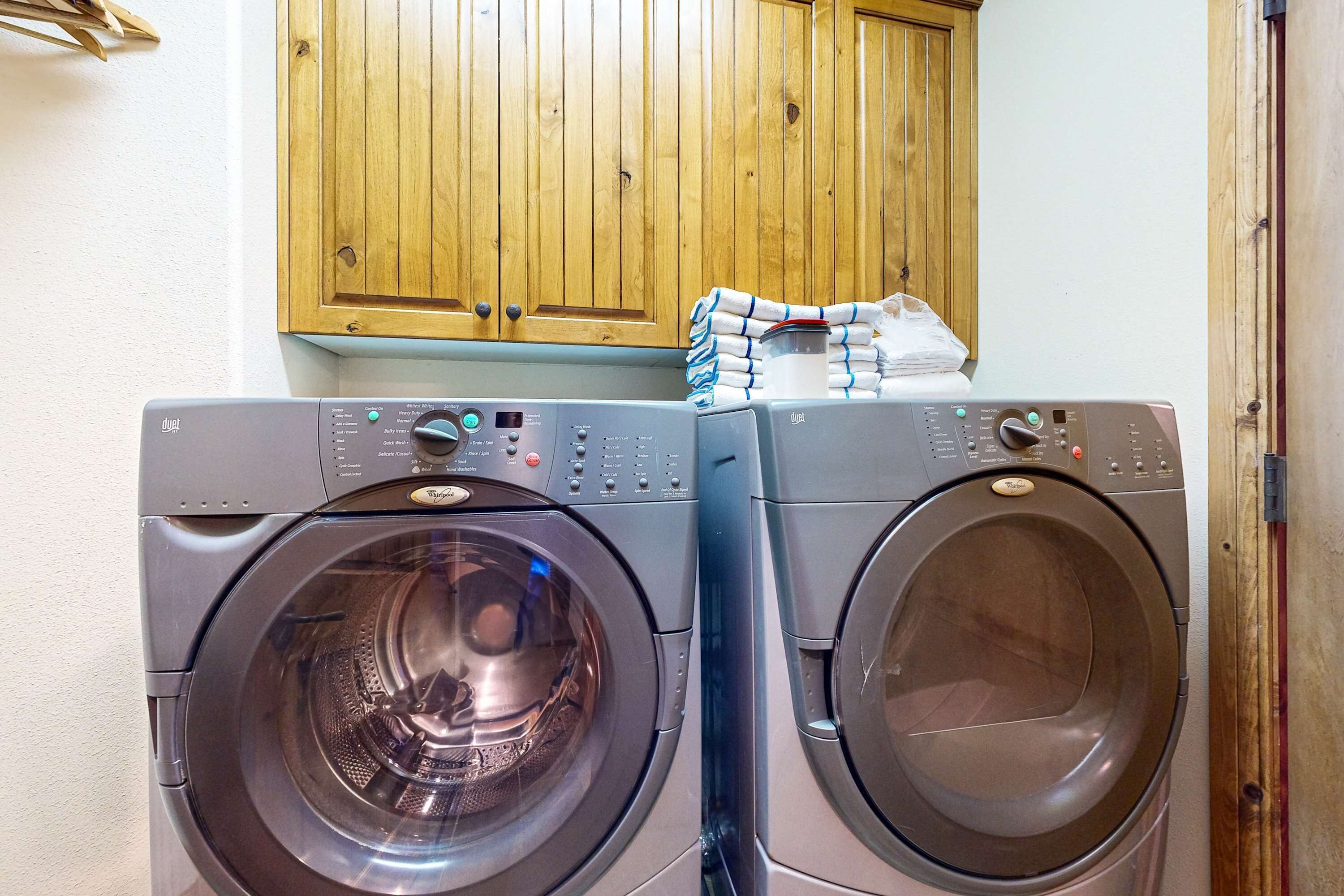 Two front-loading washing machines in a laundry area with wooden cabinets above.