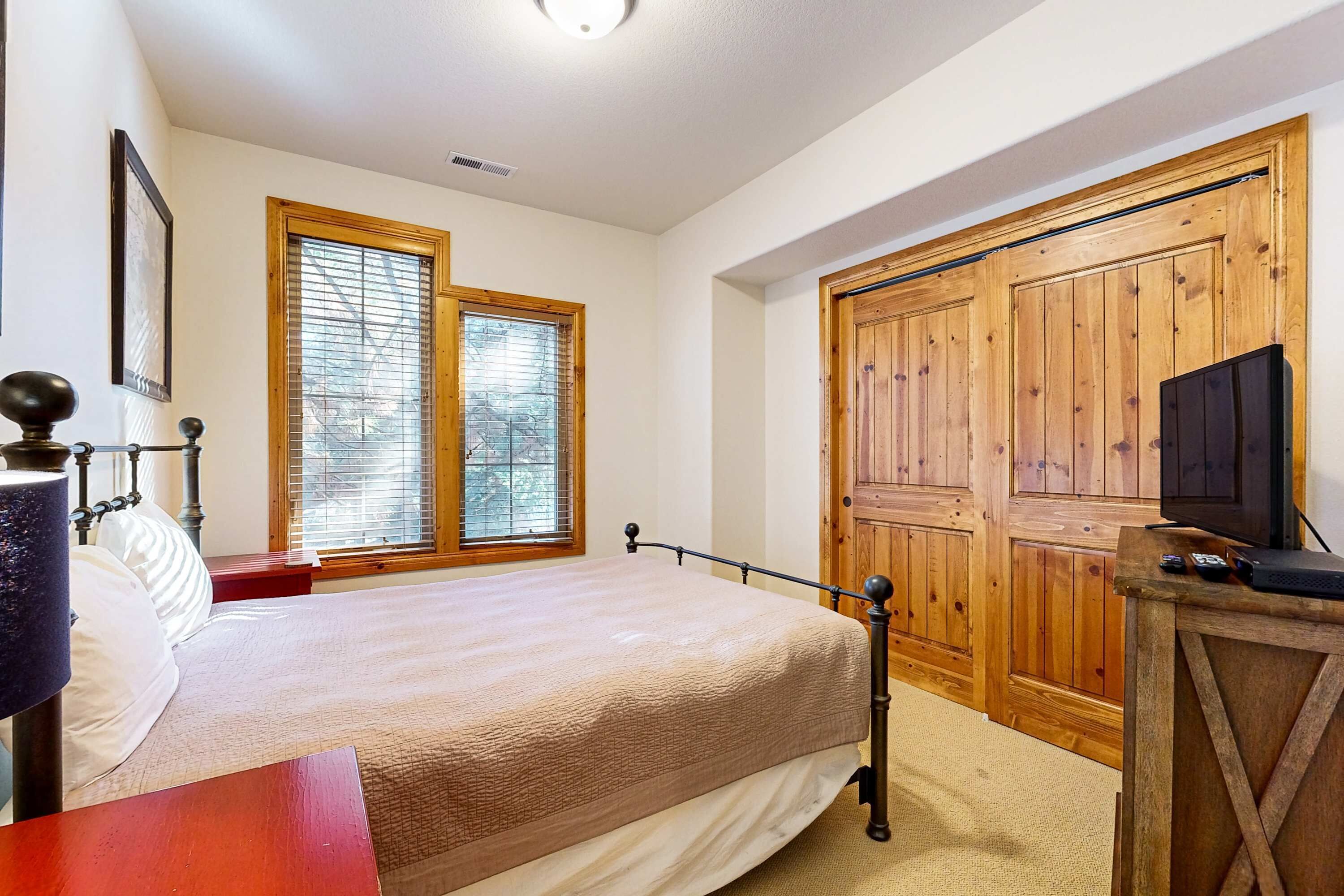 Un dormitorio con una cama, un armario de madera, un televisor sobre un mueble de madera y una ventana con persianas.