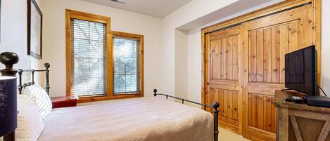 Un dormitorio con una cama, un armario de madera, un televisor sobre un mueble de madera y una ventana con persianas.