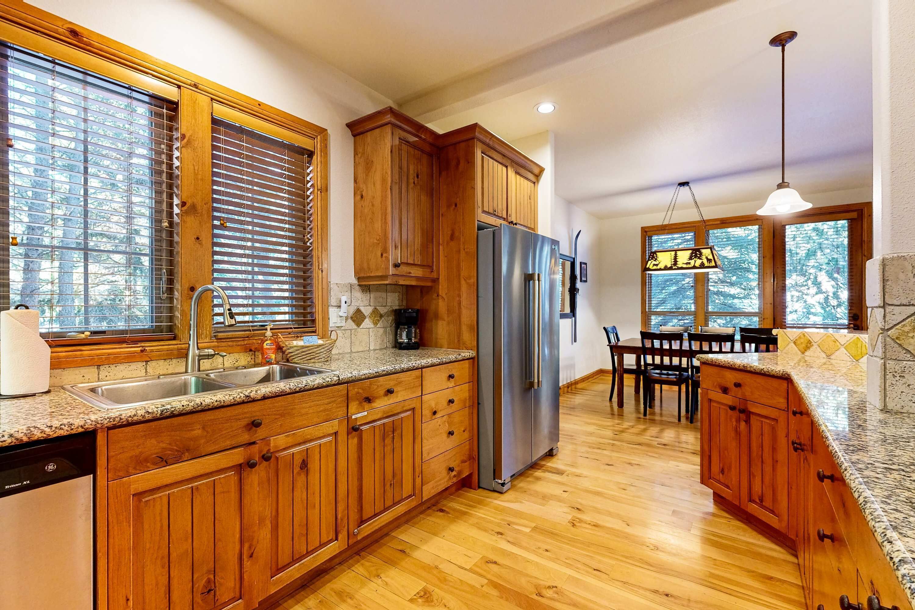 Una cocina con armarios de madera, un refrigerador de acero inoxidable, encimeras de granito y una zona de comedor con mesa y sillas.