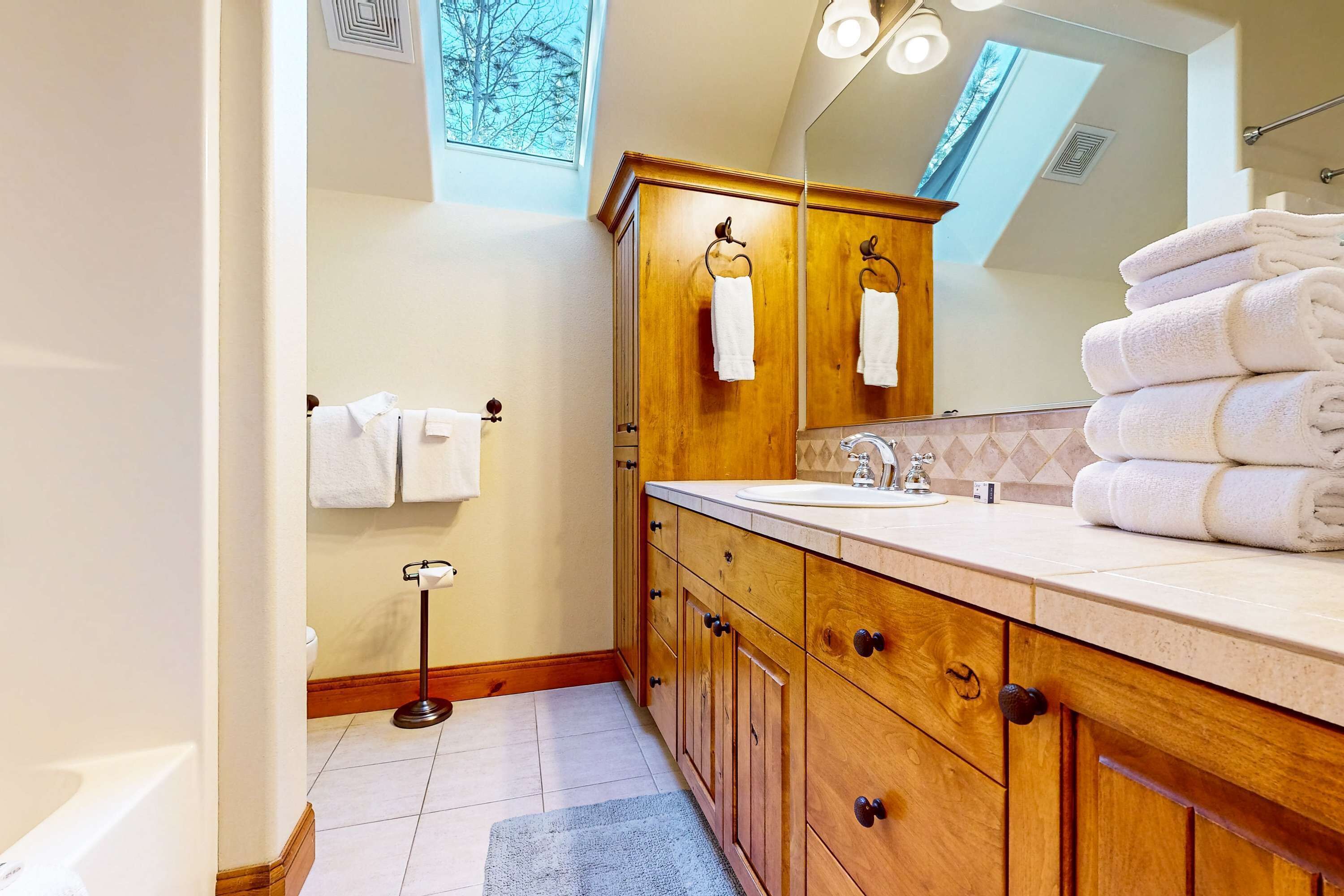 Un baño con armarios de madera, un lavabo, un espejo y una pila de toallas.