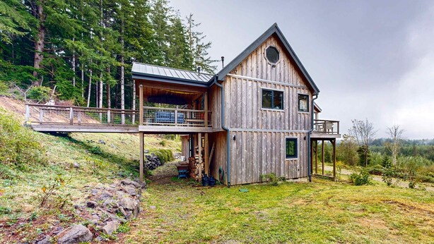 Eine Holzhütte mit Balkon, einer Veranda und Blick auf den umliegenden Wald.