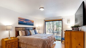 Ein Schlafzimmer mit Bett, Nachttischen, einem Fernseher, einem Fenster und Blick ins Freie.