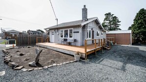 Une maison avec une terrasse en bois, une cheminée et une cour clôturée.
