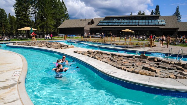 Ein Schwimmbecken mit mehreren Bahnen, Liegestühlen und einem Gebäude mit großen Fenstern im Hintergrund.