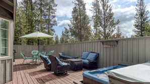 Eine Holzterrasse mit Gartenmöbeln, einem Whirlpool und Blick auf hohe Bäume.