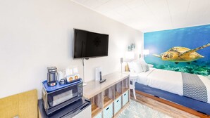 Una habitació d'hotel amb llit, televisió de pantalla plana, cafetera, microones, escriptori amb calaixos i un mural gran amb una aranyó marina.