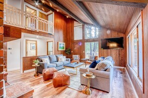 A spacious living area with a high ceiling, wooden walls, a balcony, and a television mounted on the wall. - Airy house with SHARC passes, hot tub, fireplace, central AC & bikes (Sunriver)