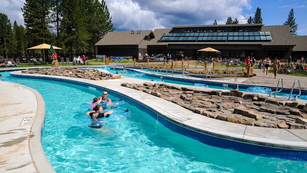 A swimming pool with multiple lanes, lounge chairs, and a building with large windows in the background. - Beautiful & spacious home with a private hot tub, fast WiFi, AC, & SHARC access (Sunriver)
