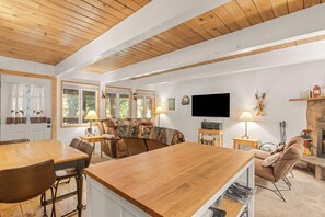 A spacious living area with a wooden ceiling, a large wooden dining table, a sofa, and a television. - Newly remodeled cabin-style condo near skiing & attractions - dogs welcome (Government Camp)