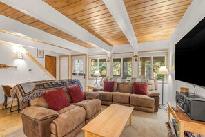 A cozy living room with a wooden ceiling, a large sofa set, a television, and a bookshelf.