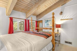 Une chambre Ă coucher avec un lit Ă baldaquin en bois, une table de chevet avec une lampe, une fenĂȘtre avec des rideaux rouges et un tableau accrochĂ© au mur.