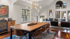 Un'ampia zona giorno con tavolo da pranzo in legno, sedie, un lampadario moderno e una grande finestra.