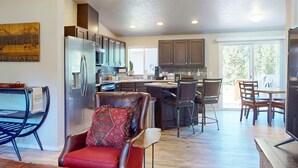A modern kitchen with a refrigerator, cabinets, and a dining area with chairs. - Cozy forest retreat near trails, slopes & Sunriver - perfect for year-round fun! (Bend)