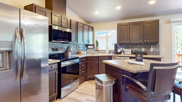 A modern kitchen with stainless steel appliances, dark wooden cabinets, and a central island with bar stools. - Cozy forest retreat near trails, slopes & Sunriver - perfect for year-round fun! (Bend)