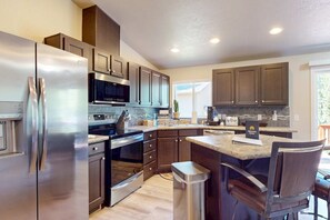 A modern kitchen with stainless steel appliances, dark wooden cabinets, and a central island with bar stools. - Cozy forest retreat near trails, slopes & Sunriver - perfect for year-round fun! (Bend)