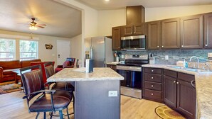 A modern kitchen with dark wood cabinets, stainless steel appliances, and a granite countertop. - Cozy forest retreat near trails, slopes & Sunriver - perfect for year-round fun! (Bend)