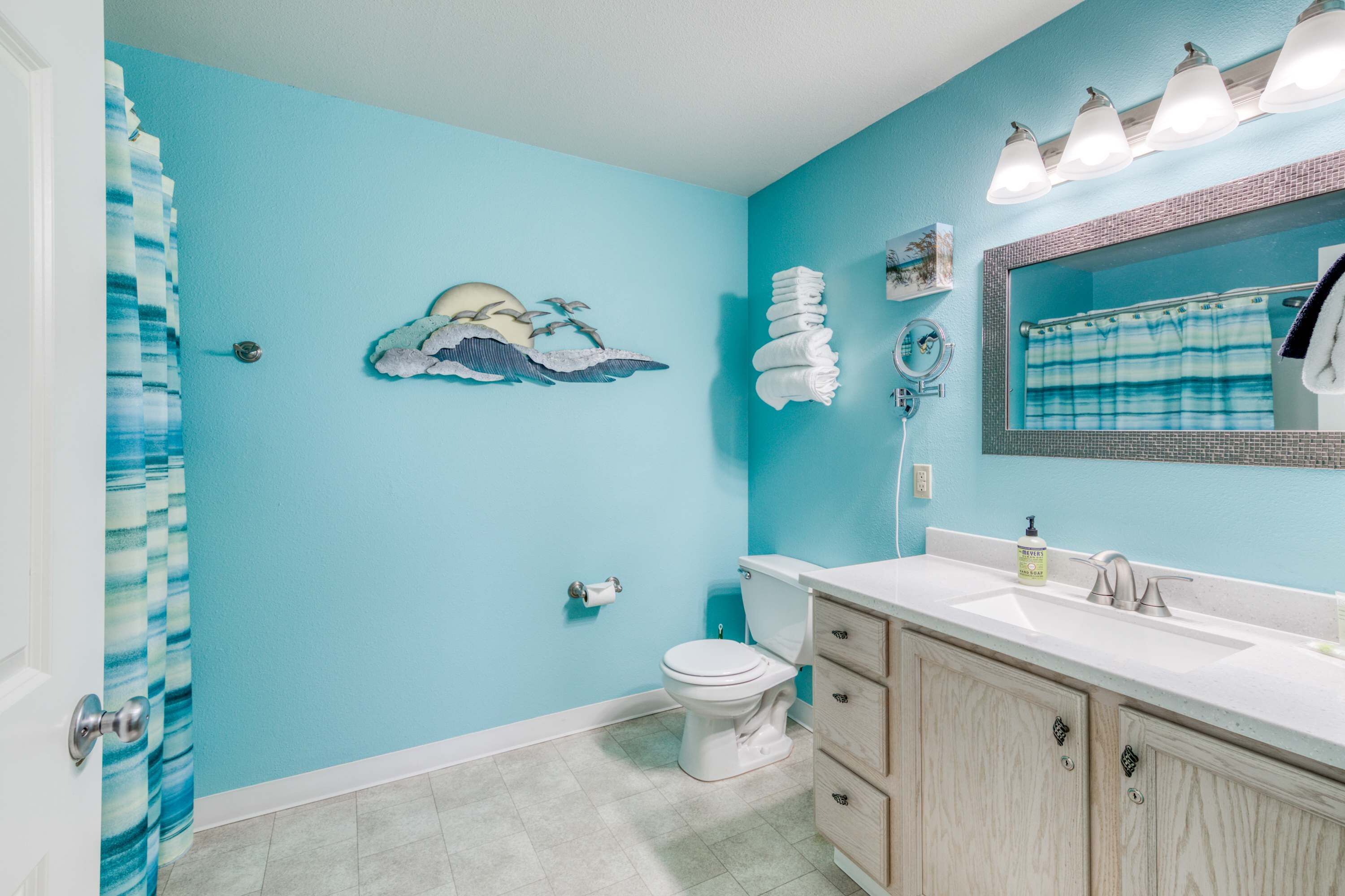 Un baño con pared azul, inodoro, lavabo con espejo y cortina de ducha.