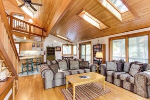 A spacious living area with a wooden ceiling, a sofa set, a coffee table, and a kitchen in the background. - Cute Cottage with Close Beach Access & Free WiFi - Dogs Welcome (Cannon Beach)