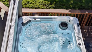 Un jacuzzi en una terraza de madera con vistas a un césped cuidado.