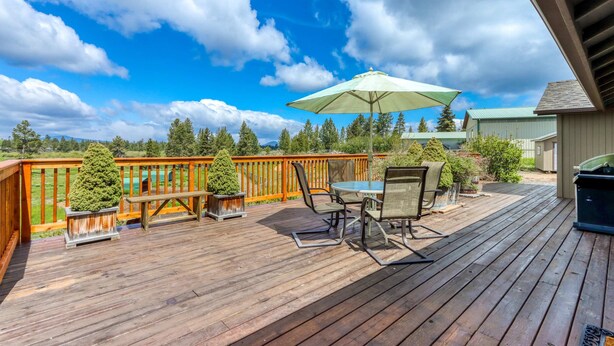Eine Holzterrasse mit Tisch, Stühlen und einer Bank, sowie ein großer Sonnenschirm.